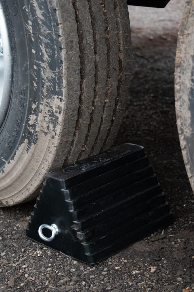 Black rubber wheel chock stabilizing vehicle tires for safety and convenience.
