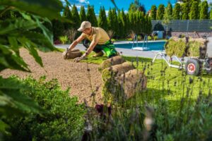 Gardener laying sod for a lush lawn transformation near a swimming pool.