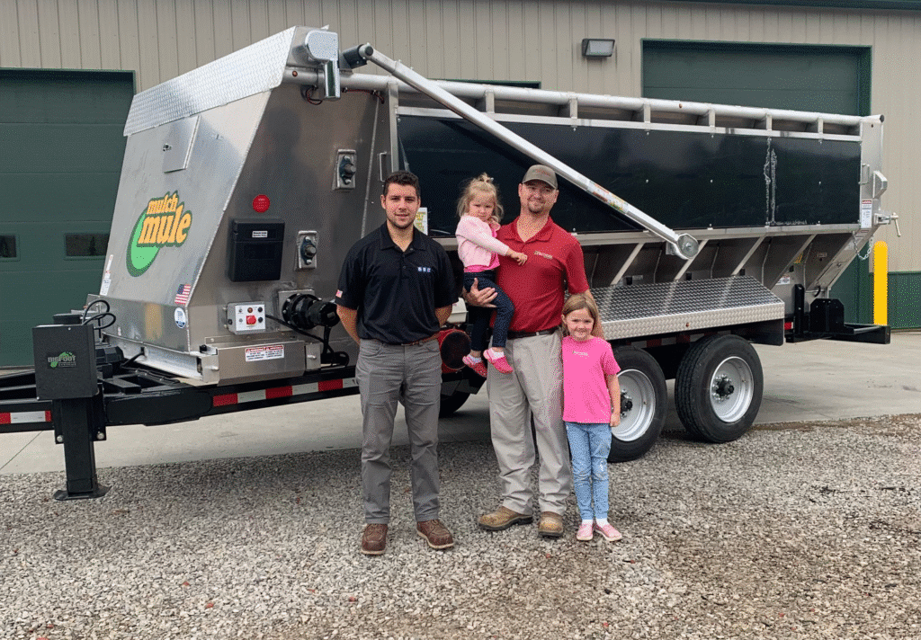 Family and team standing proudly with Mulch Mule agricultural equipment in front of a facility.
