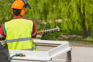 Landscaping worker using hedge trimmer while wearing safety gear in a lush environment.
