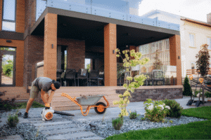 A gardener enhances a modern backyard with plants and landscaping tools.