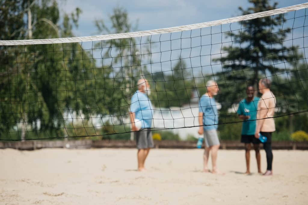 Interracial group of older men discussing volleyball by the sand volleyball net