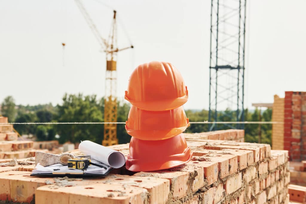 Protective hard hats on bricks at a construction site with cranes in the background.