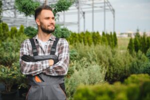 Gardener standing confidently among lush greenery in a plant nursery.