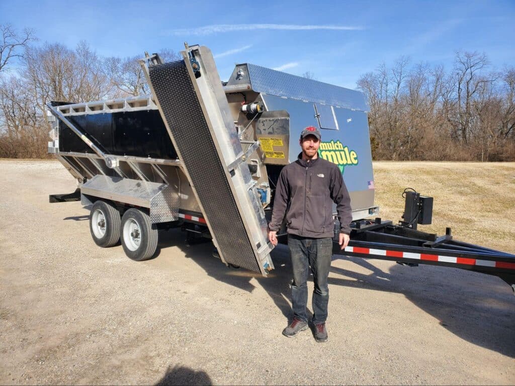 Man standing beside heavy-duty Mulch Mule trailer, showcasing commercial equipment for landscaping and construction.