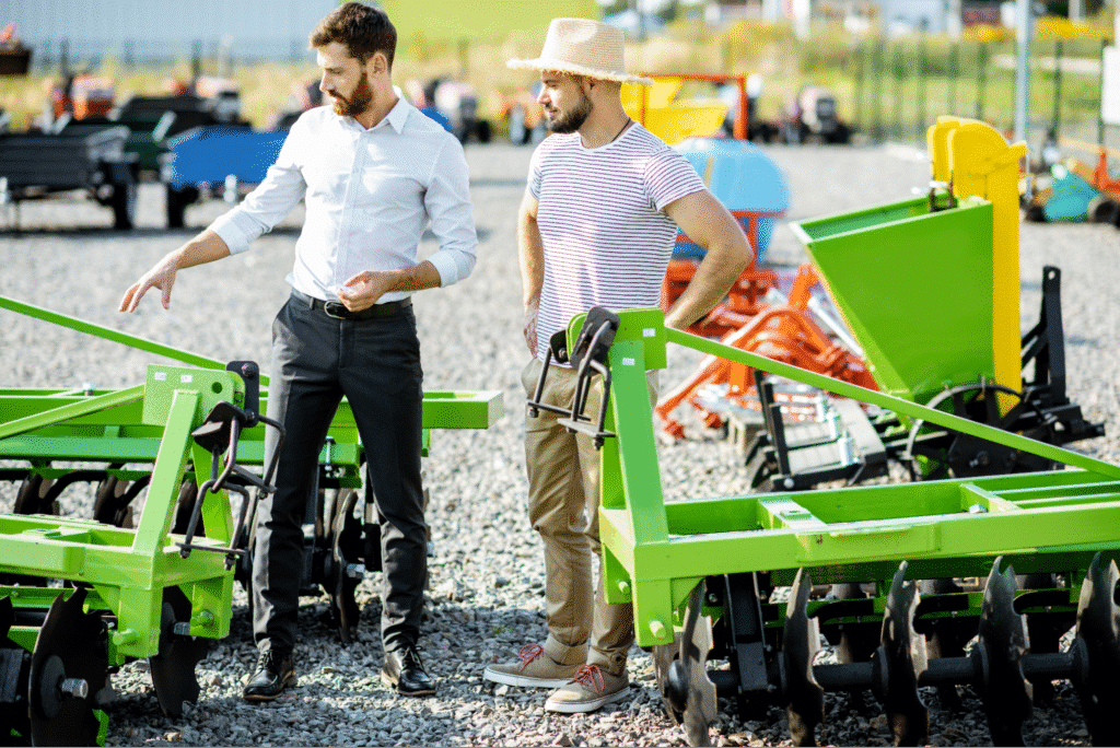 Farmers discussing new agricultural equipment at an outdoor machinery dealership.