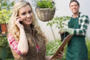 Woman on phone in a garden center sharing plant care advice with a friend.