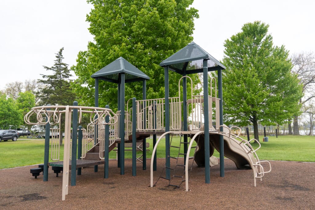 Modern playground equipment in a public park surrounded by lush green trees.