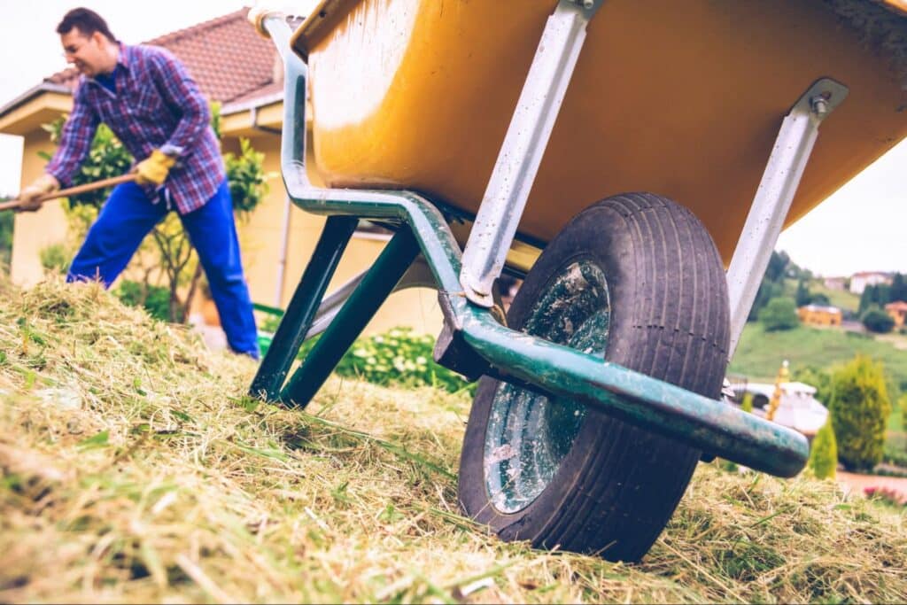 Man using a wheelbarrow for gardening and landscaping in a backyard setting.