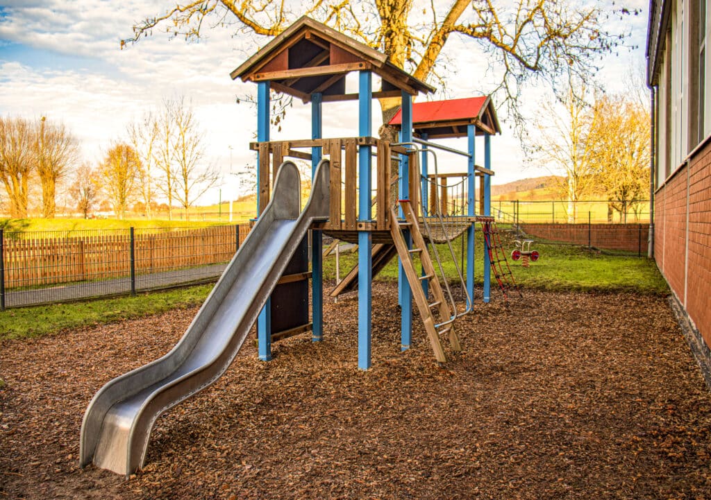 Metal slide on a colorful wooden playground surrounded by grass and trees.