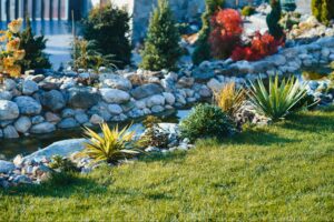 Lush garden landscape with colorful plants and decorative stones near a serene water feature.