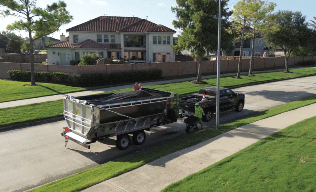 Mulch Mule bulk mulch equipment trailer in suburban neighborhood with beautiful homes and lush greenery.
