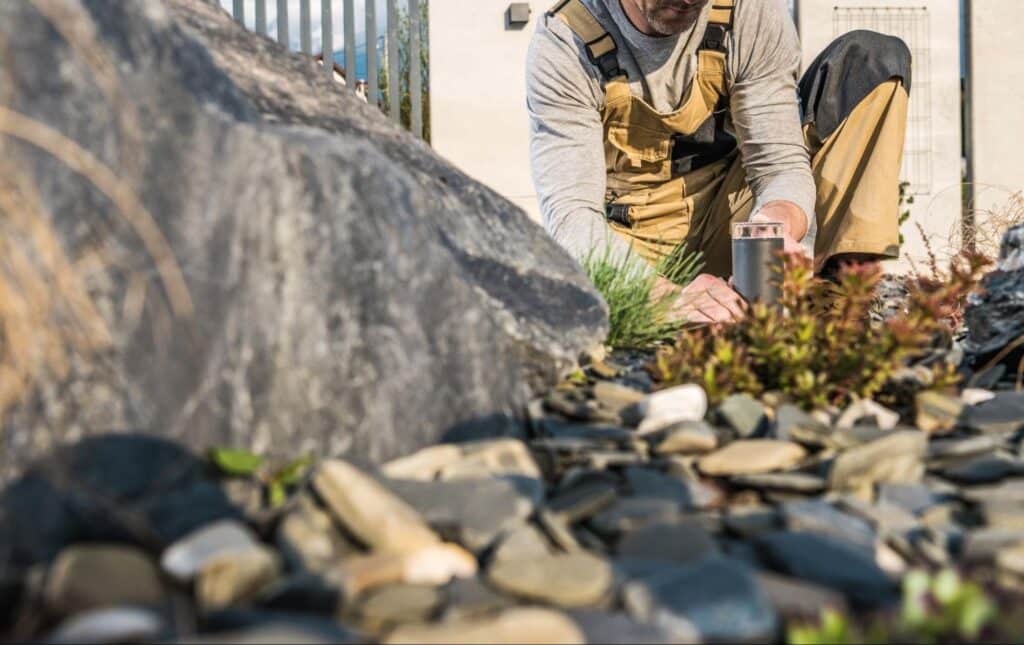 Gardener tending to plants and stones in a landscaped garden setting.