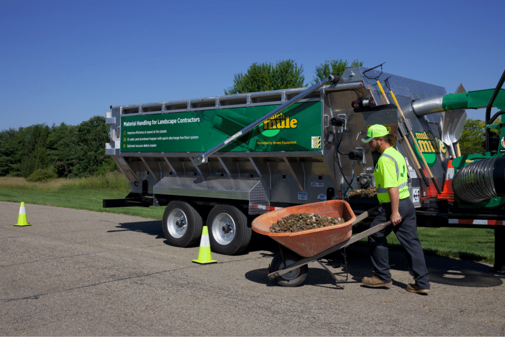 Worker using a wheelbarrow to transport material near a Mulch Mule trailer demonstrating 5s methodology