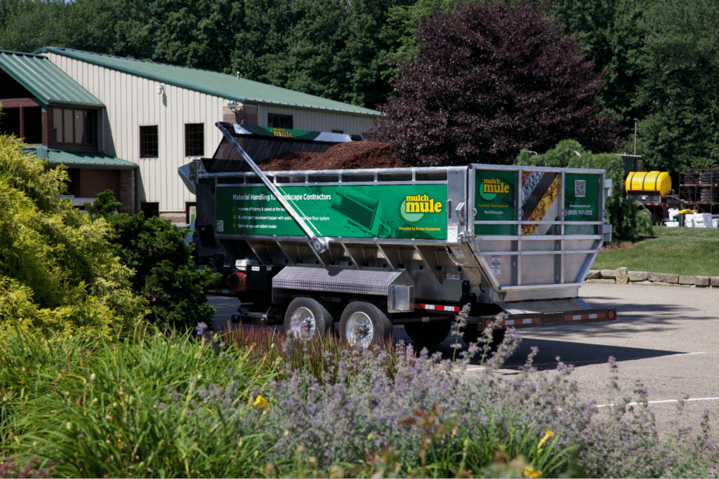 Green Mulch Mule landscaping trailer parked outside, showcasing plants and gardening equipment.