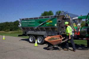 Worker using a wheelbarrow near a landscaping machine on a sunny day.