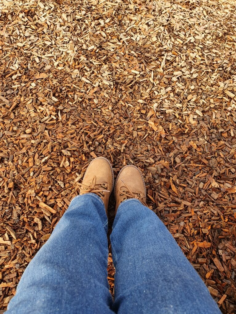 Travelers legs in hiking boots on bark ground, ready for adventure.