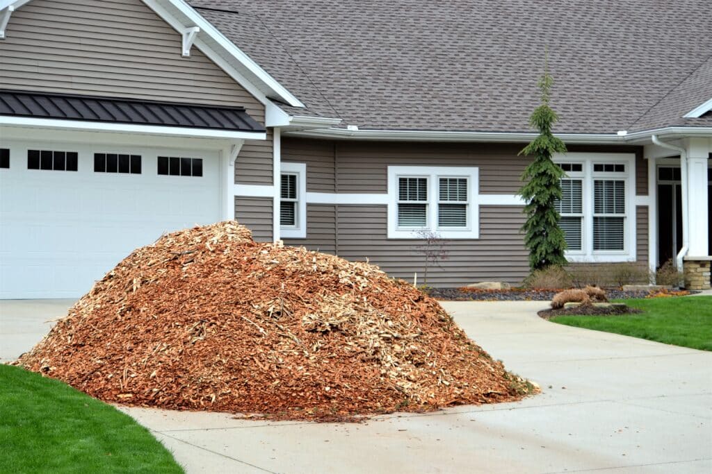 A large pile of wood chips near a residential home.