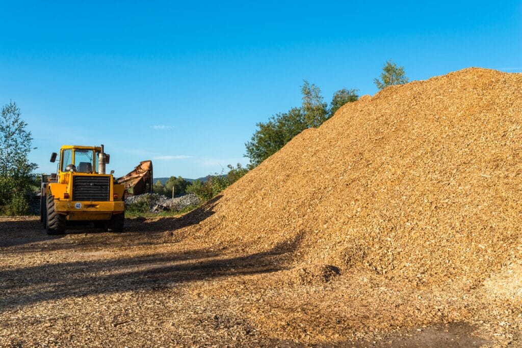 Yellow loader moving wood chips at a landscaping site under a clear blue sky.