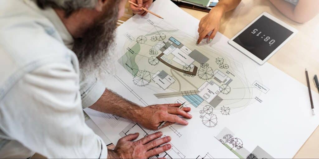 Hands collaborating over architecture blueprints with a digital timer nearby.