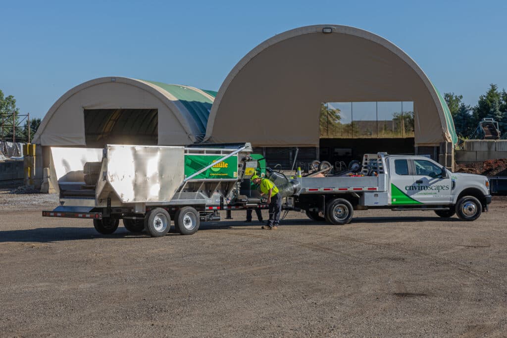 A worker loads materials onto a trailer for landscaping equipment transport.